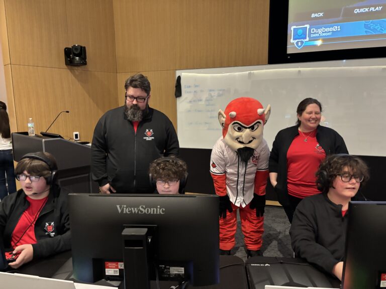 Students playing a video game while a man and woman coach watch